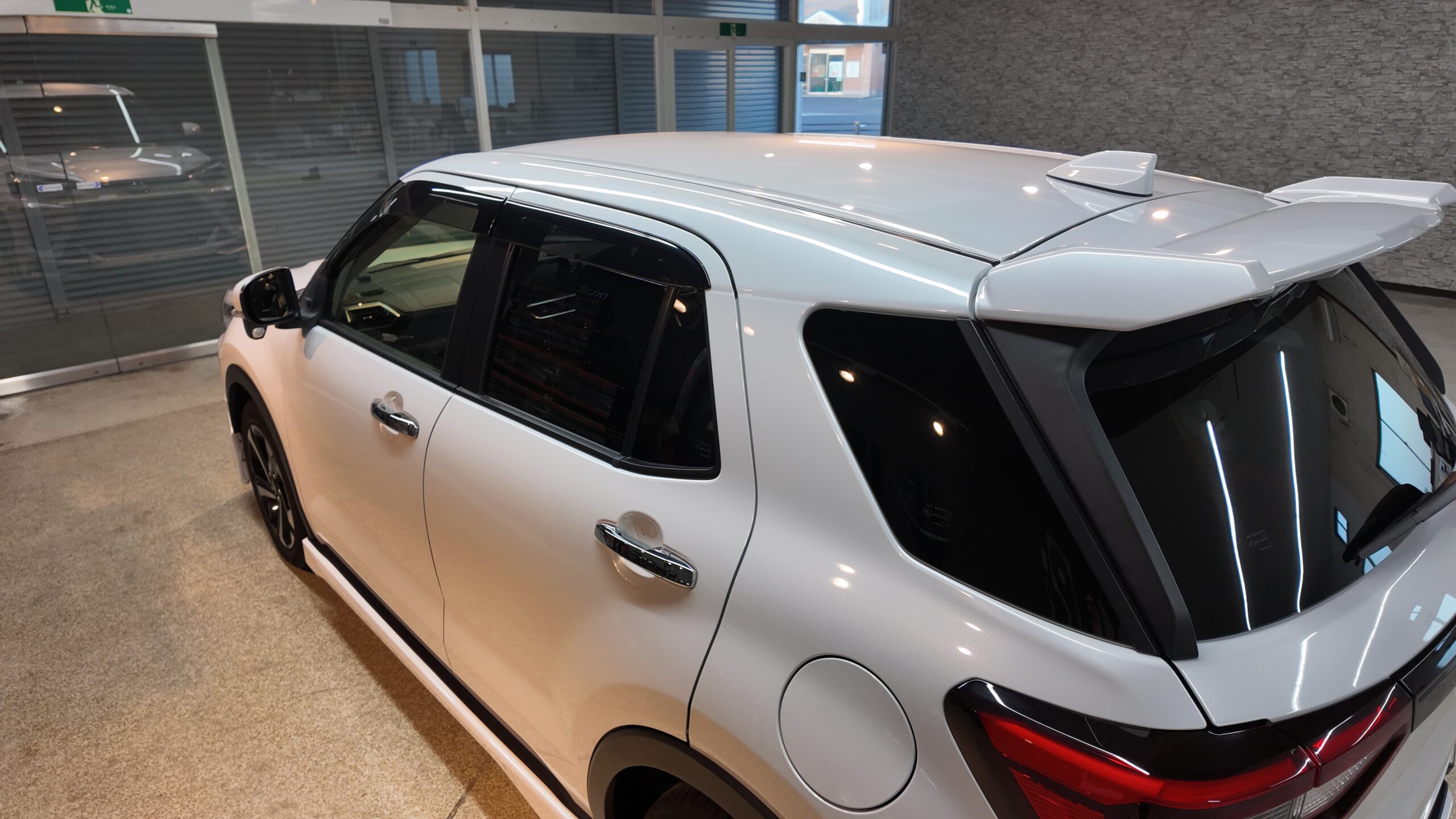 Silver SUV parked indoors in showroom, rear quarter panel visible with spoiler and tinted rear window.