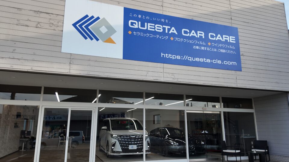 Blue storefront sign reading 'GUESTA CAR CARE' with Japanese text, above a glass showroom showing white cars inside.