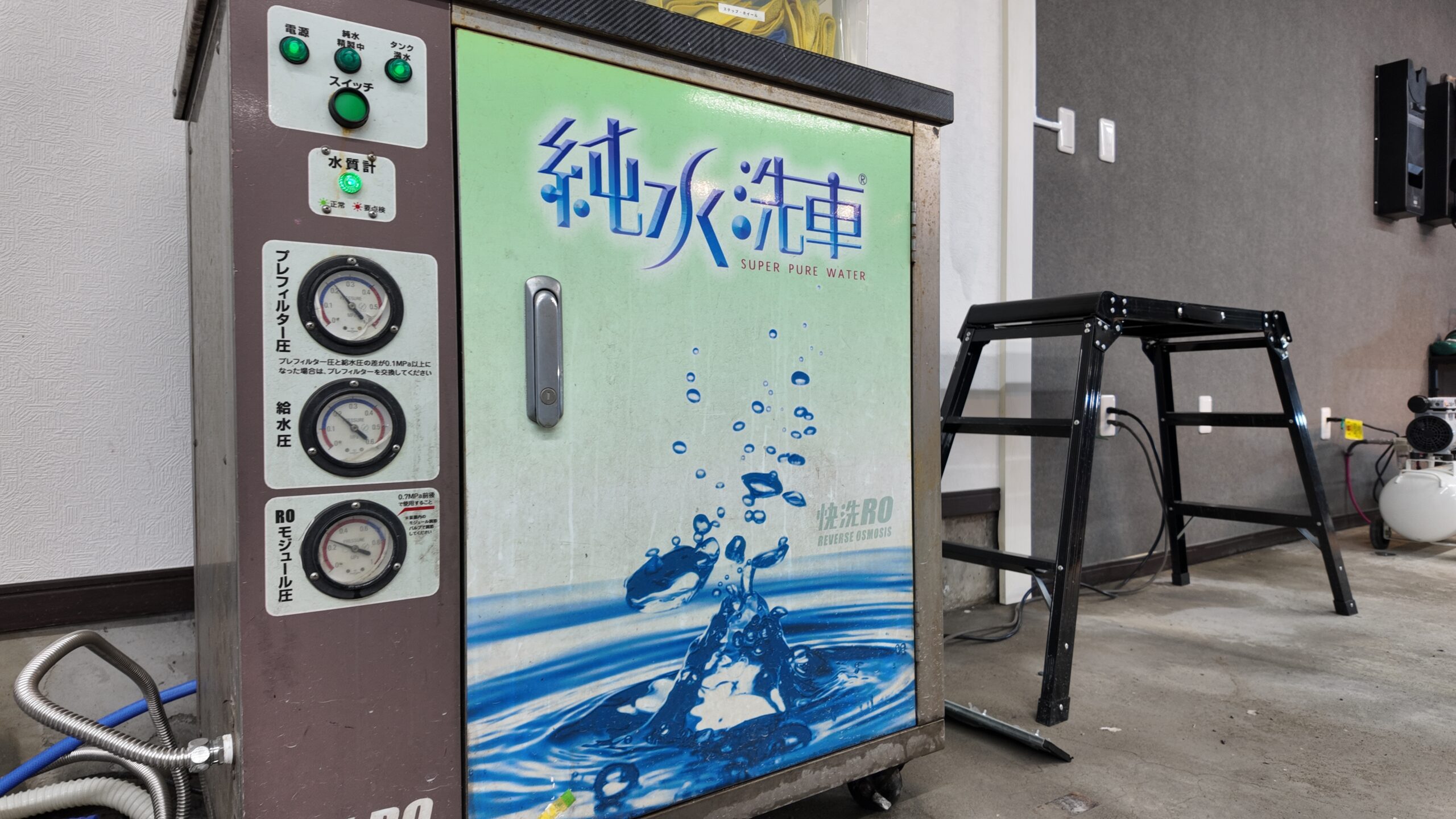 Industrial water purification vending machine with gauges and hoses, mint-green panel reading 'Super Pure Water' and blue splash design, in a workshop setting.