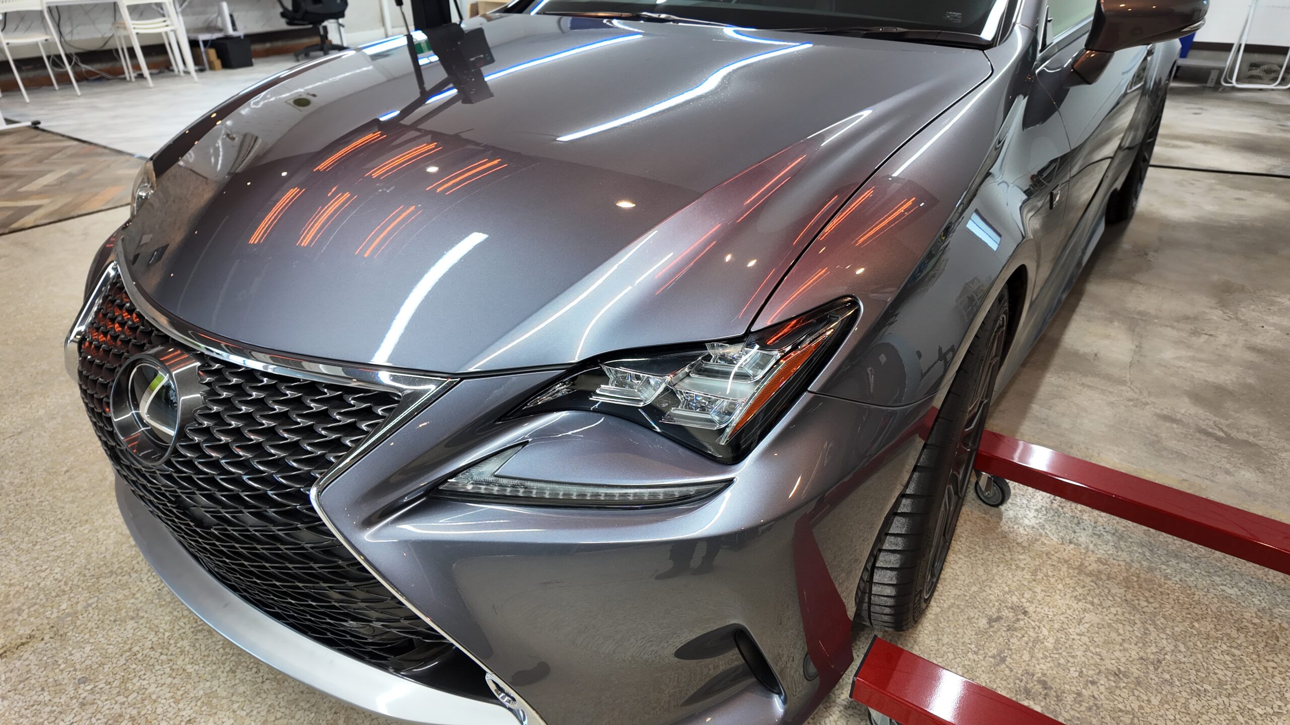 Front-left view of a gray Lexus sedan with a prominent spindle grille in a workshop setting.