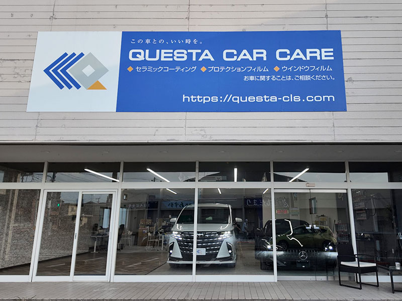 Exterior of QUESTA CAR CARE storefront with a blue sign and logo; glass doors reveal a white van and a black car inside the showroom.