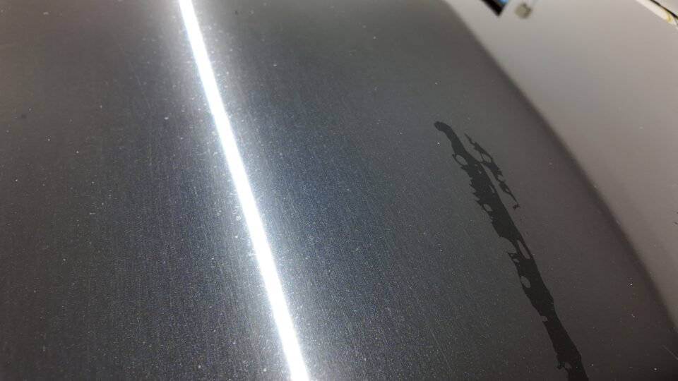 ボディーのシミ - QUESTA CAR CARE 千葉県君津市のコーティングプロショップ Close-up of a dark metallic car hood with a bright vertical reflection stripe and scattered dust particles.