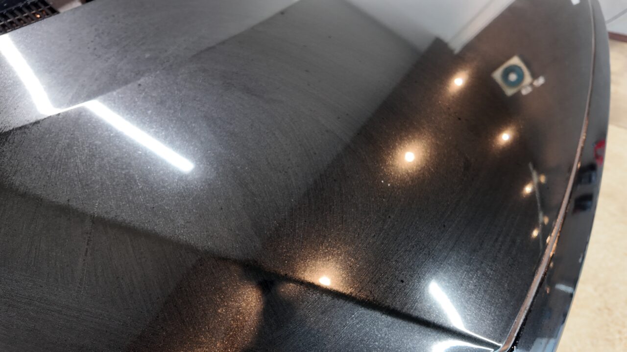 - QUESTA CAR CARE 千葉県君津市のコーティングプロショップ Close-up of a glossy black car roof with dust specks and overhead light reflections in a curved surface edge.
